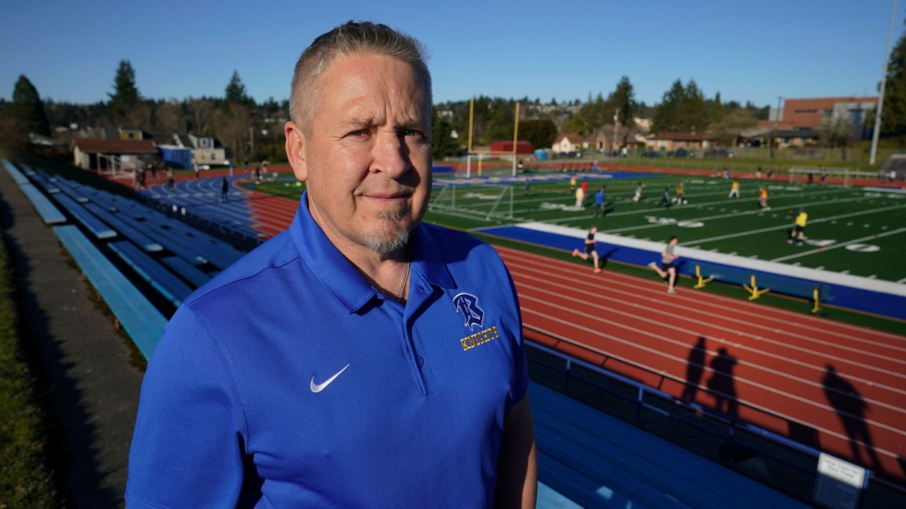 Joe Kennedy, a former assistant football coach at Bremerton High School in Bremerton, Wash., poses for a photo March 9, 2022, at the school's football field. After losing his coaching job for refusing to stop kneeling in prayer with players and spectators on the field immediately after football games, Kennedy will take his arguments before the U.S. Supreme Court on Monday, April 25, 2022, saying the Bremerton School District violated his First Amendment rights by refusing to let him continue praying at midfield after games. 