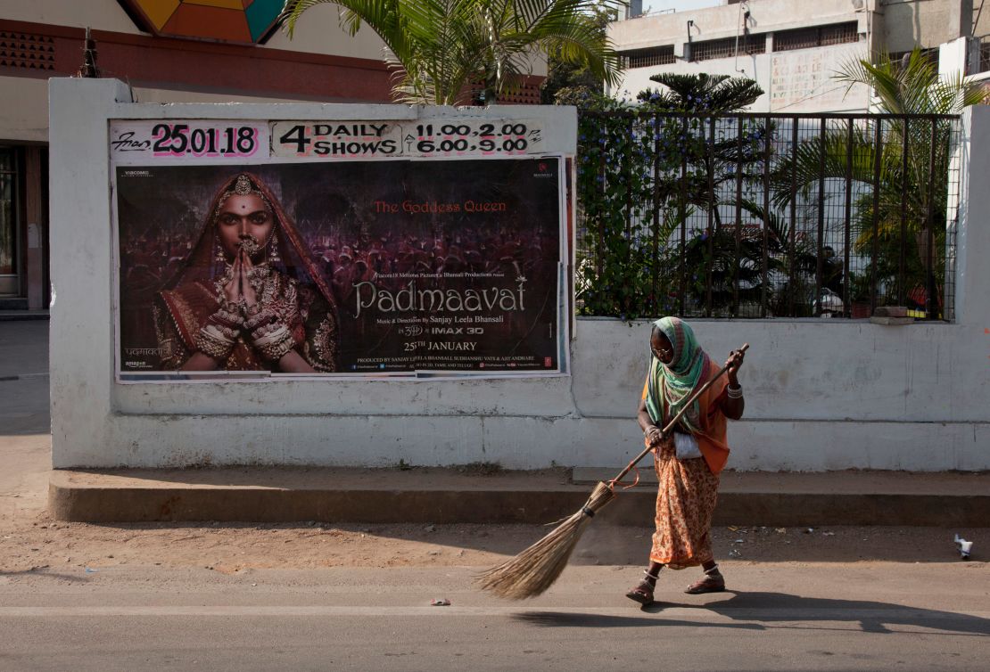 An Indian municipal worker sweeps a street in front of a poster of Bollywood film "Padmaavat" outside a movie theatre in Hyderabad, India in 2018.