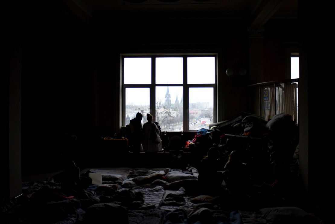 Families, their belongings stacked in piles around them, look out over the entrance to Lviv train station. Outside, lines of buses take refugees to the Polish border.