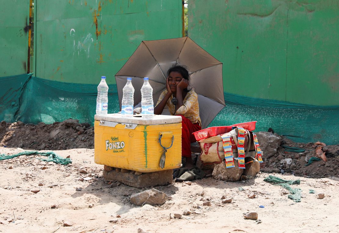 A girl selling water uses an umbrella to protect herself from the sun in New Delhi.