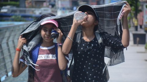Girls cover their heads as they walk and drink water in the scorching afternoon heat in Mumbai.