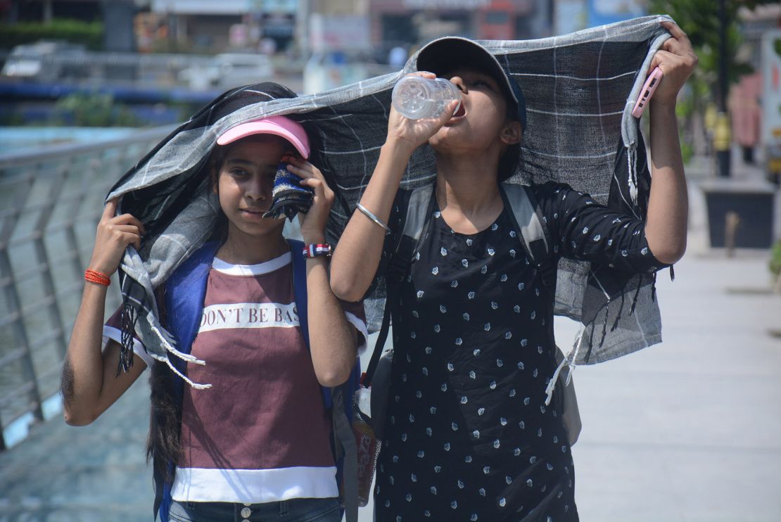 Girls cover their heads as they walk and drink water in the scorching afternoon heat in Mumbai.
