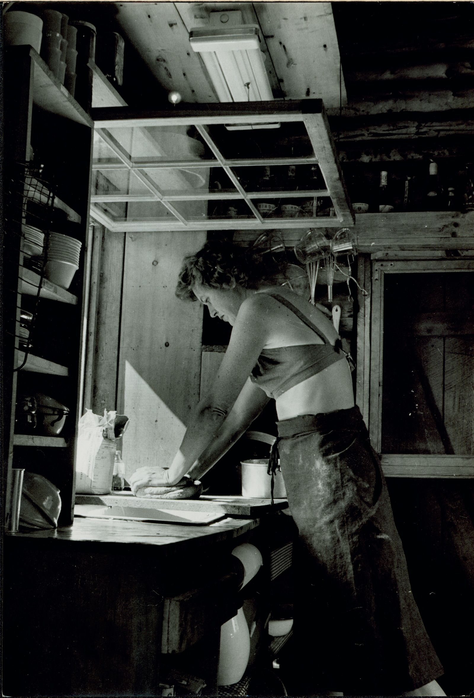 Child kneads dough by an open kitchen window in a cabin in Maine, circa 1952.