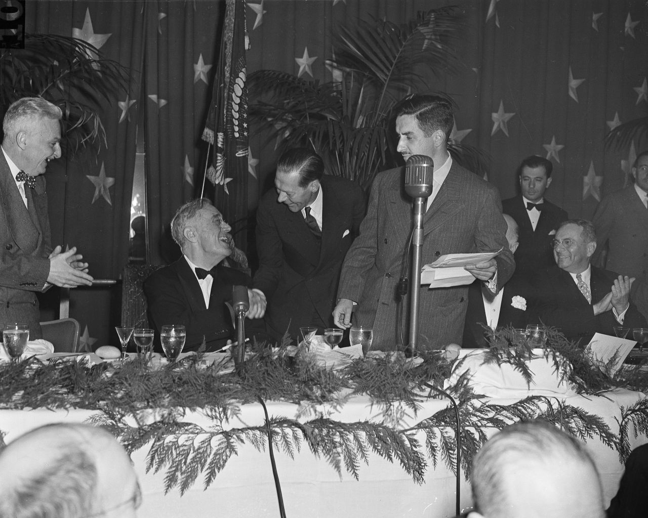 President Franklin D. Roosevelt, seated, shakes hands with Raymond P. Brandt, chief of the Washington bureau of the St. Louis Post-Dispatch, at the 1945 dinner. Roosevelt was congratulating Brandt for winning the first Raymond Clapper Memorial Award, which was given by the White House Correspondents' Association for distinguished reporting.