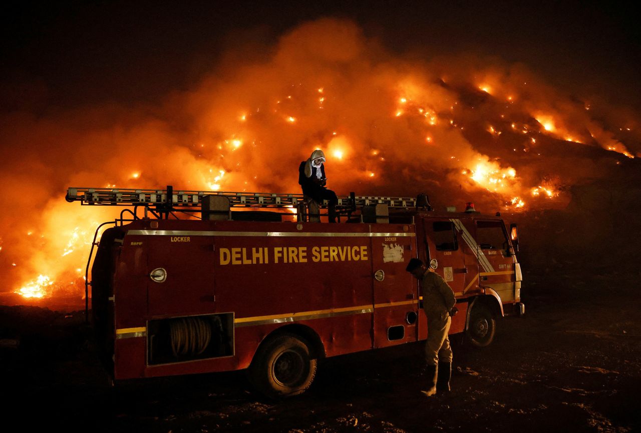 A firefighter uses his cell phone on top of a truck Wednesday, April 27, as smoke billows from the Bhalswa landfill site that caught fire in New Delhi.