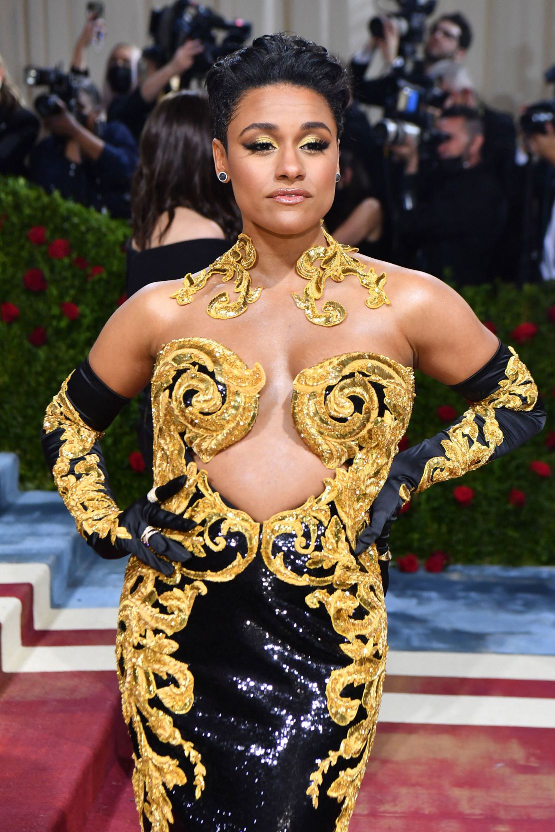 West Side Story star Ariana DeBose added a dose of glamour to her black and golden Moschino outfit with a pair of opera gloves and jewelry inspired by her gown's swirling motif. 