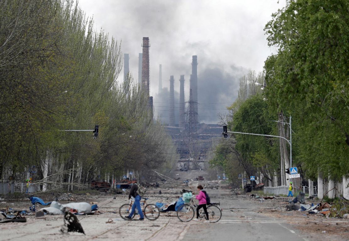 People walk their bikes across the street as smoke rises above a plant of the Azovstal steel plant in Mariupol, Ukraine, on May 2. 