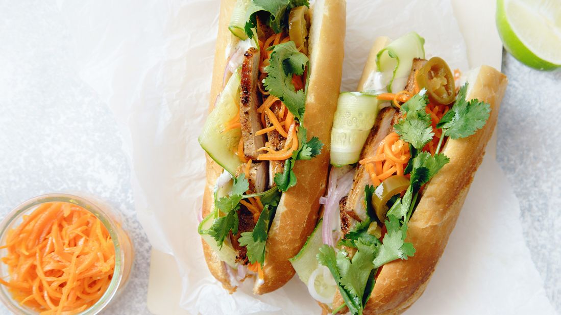 <strong>Bánh mì, Vietnam:</strong> Classical bánh mì sandwich with sliced grilled pork tenderloin, shredded carrots and peeled cucumbers, jalapeno peppers and cilantro on white textured background.