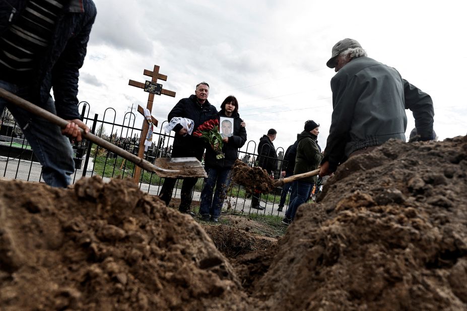 Maria, 13, holds a photograph of her father, Yurii Alekseev, as she and her godfather, Igor Tarkovskii, attend Alekseev's funeral in Bucha, Ukraine, on April 26. Alekseev, 50, was a territorial defense member who was killed by Russian soldiers, according to his family.