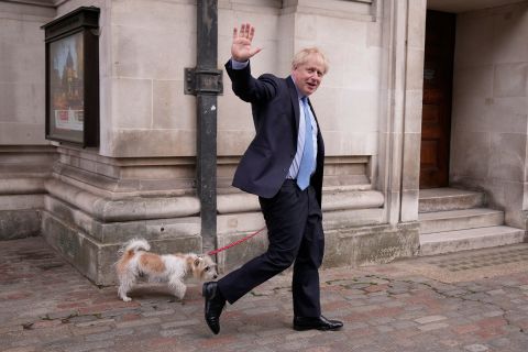 British Prime Minister Boris Johnson — accompanied by his dog, Dilyn — waves at the media after he voted at a polling station in London on Thursday, May 5. <a href=
