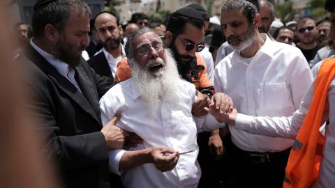 Ultra-Orthodox Jewish mourners circle a man overcome with grief following the attack.