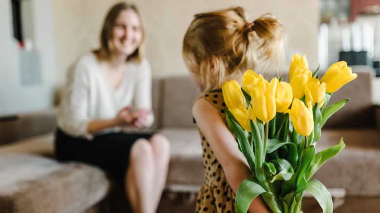 Cute little girl greeting mother and gives her a bouquet of flowers tulips at home for Mother's Day.
