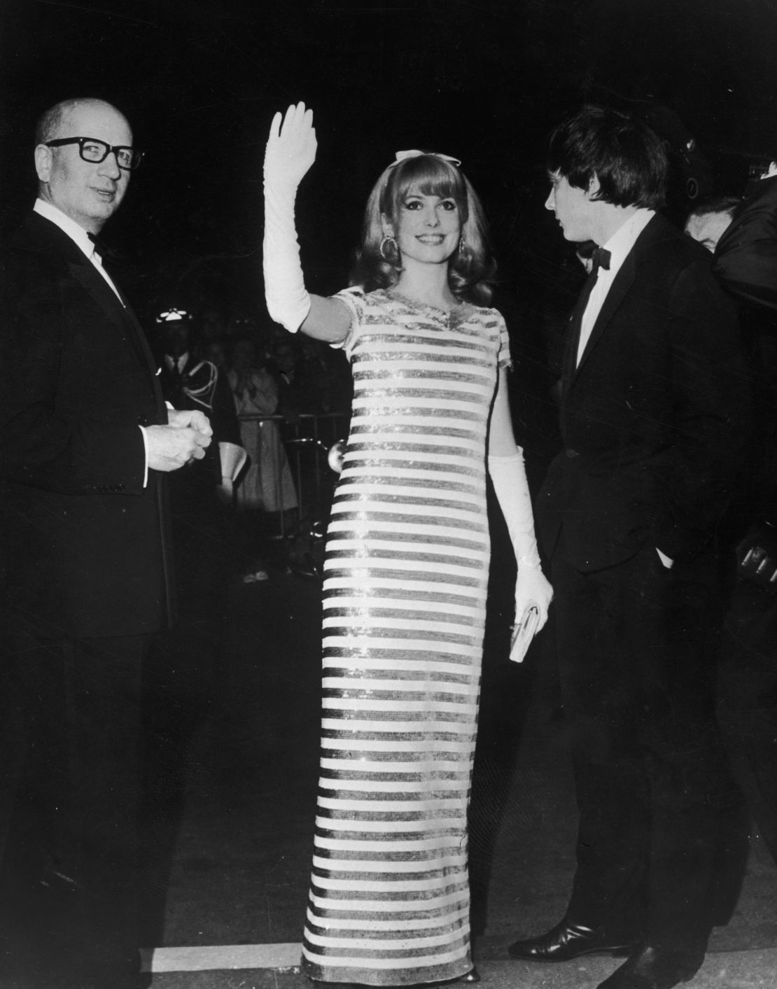French actress Catherine Deneuve greets her fans in white gloves and sequins at the 1966 Cannes Film Festival. 