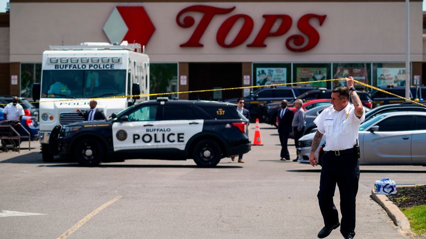 A police officer lifts the tape cordoning off the scene of a shooting at a supermarket, in Buffalo, N.Y., Sunday, May 15, 2022. A white 18-year-old wearing military gear and livestreaming with a helmet camera opened fire with a rifle at a supermarket in Buffalo, killing and wounding people in what authorities described as "racially motivated violent extremism." 