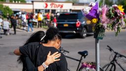 BUFFALO, NY - MAY 15: Jeanne LeGall, of Buffalo, hugs Claudia Carballada, of Buffalo, as she gets emotional, as she pays her respects at an makeshift memorial as people gather at the scene of a mass shooting at Tops Friendly Market at Jefferson Avenue and Riley Street on Sunday, May 15, 2022 in Buffalo, NY. The fatal shooting of 10 people at a grocery store in a historically Black neighborhood of Buffalo by a young white gunman is being investigated as a hate crime and an act of racially motivated violent extremism, according to federal officials. (Kent Nishimura / Los Angeles Times via Getty Images)