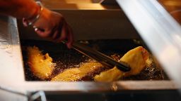 A chef turns a piece of fried fish in the fryer as it gets cooked, at Captain's Fish and Chip shop in Brighton on March 25, 2022. - Britain's fish and chip shops have weathered the storm of Brexit and Covid, and are fighting the tide of rising inflation but thousands could be sunk by the war in Ukraine. At Captain's in the seaside resort of Brighton, on England's south coast, owner Pam Sandhu is not one to normally complain. Yet the shelves of her large freezers are empty when they should be full of white fish ready to be dipped in batter and deep fried, then served to hungry customers with piping hot chips. "With the war in Ukraine, there's no fish left, only a small amount," she told AFP. "And prices have doubled since last year." (Photo by ADRIAN DENNIS / AFP) (Photo by ADRIAN DENNIS/AFP via Getty Images)