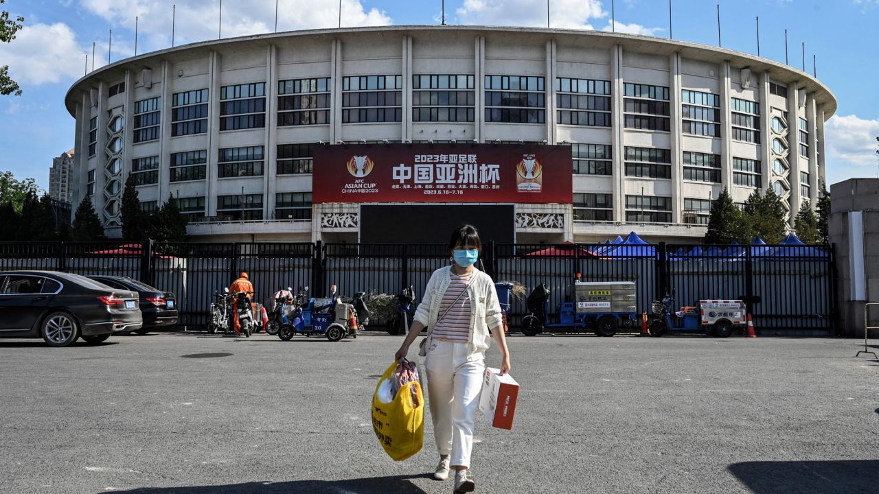 A woman walks in front of a building with a billboard promoting the now moved 2023 Asian Cup in Beijing on May 14, 2022.