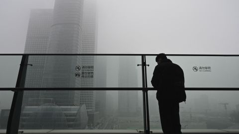 A man stands next to a glass wall on a balcony on a polluted day in Beijing on November 5, 2021. 