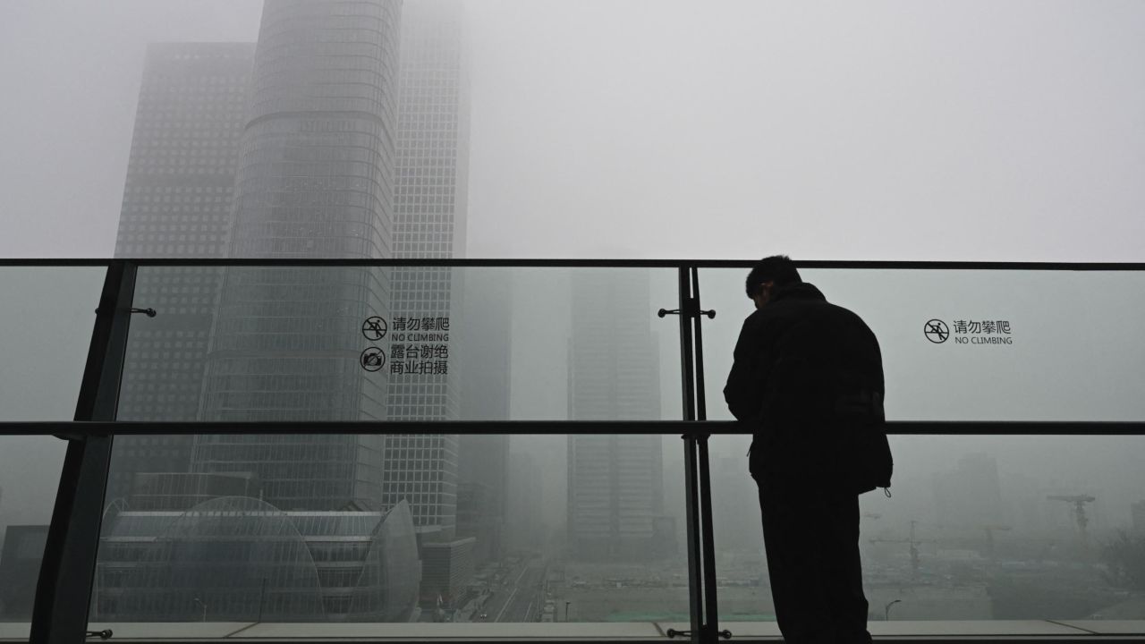 A man stands next to a glass wall on a balcony on a polluted day in Beijing on November 5, 2021.