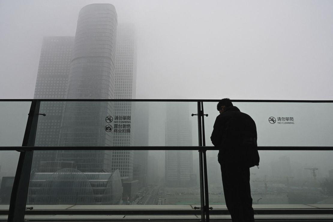 A man stands next to a glass wall on a balcony on a polluted day in Beijing on November 5, 2021. 
