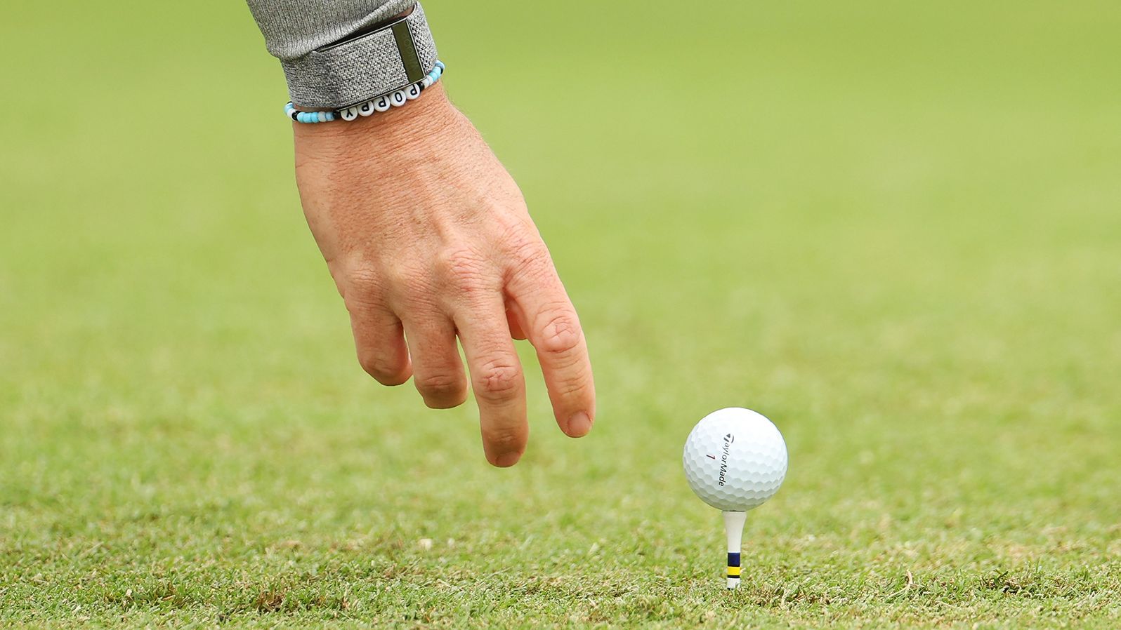 Rory McIlroy places his golf ball on the fourth tee wearing a bracelet with his daughter's name on it.