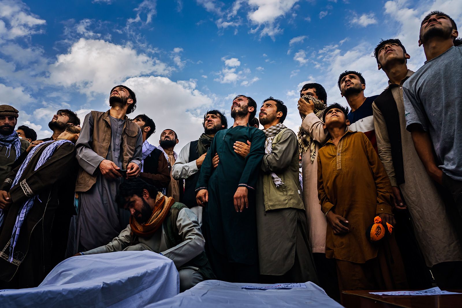 August 30, 2021: Attendees at a funeral look up and sob as the sound of engines roars over their cries in Kabul. They mourn a family burying ten of their own, seven of them children, after a U.S. airstrike left devastation in its wake.