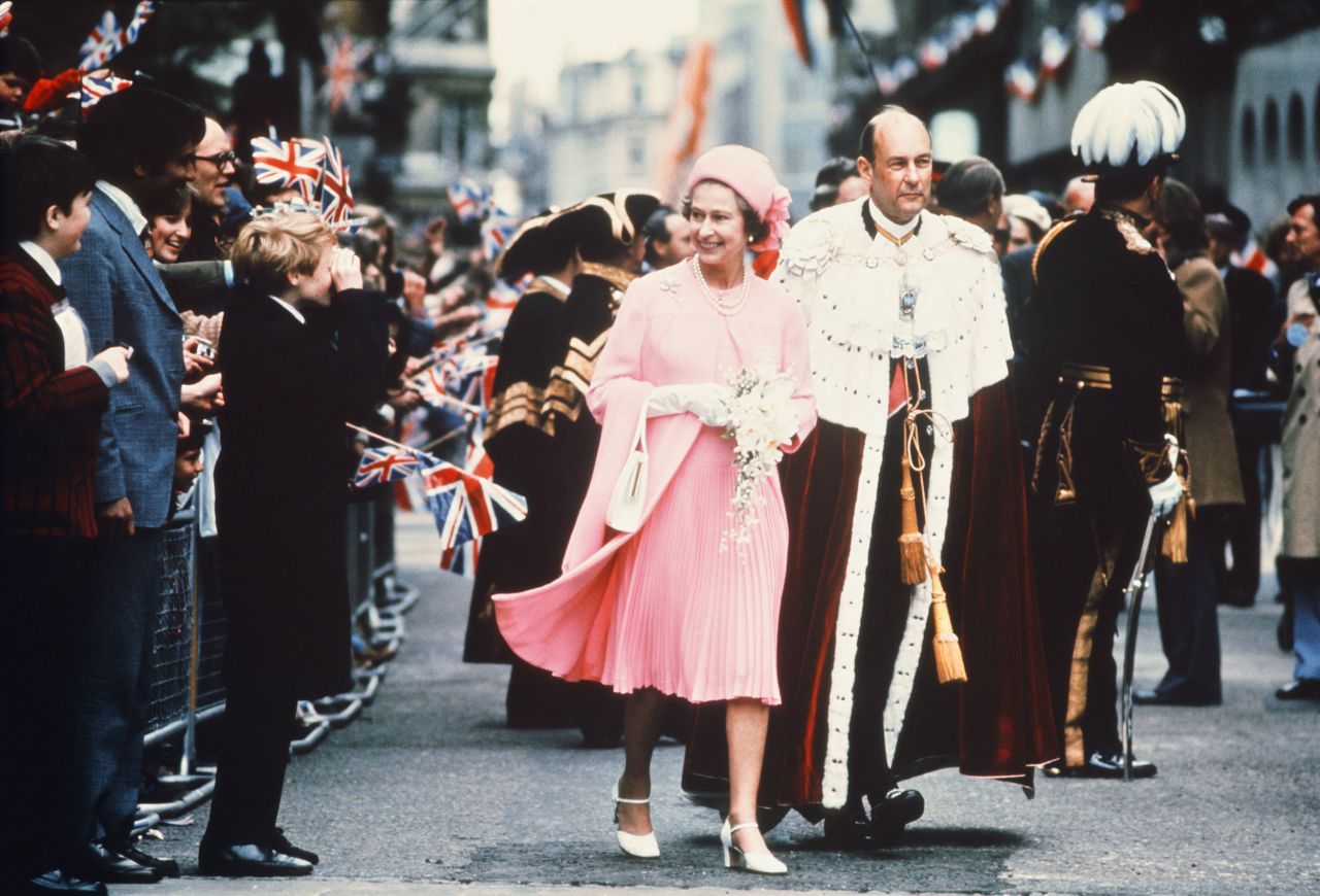 Flag-waving crowds greet the Queen as she walks to the Guildhall for lunch, following the Silver Jubilee thanksgiving service. She is accompanied by then-Lord Mayor of London Robin Gillett.