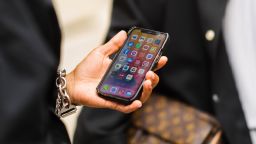 A guest wears silver bracelet, holds in his hand an iPhone unlocked on the application screen, outside Officine Générale, during Paris Fashion Week - Menswear Spring/Summer 2022, on June 25, 2021 in Paris, France. 