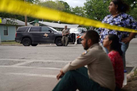 People sit on the curb outside of the school as state troopers guard the area on May 24.