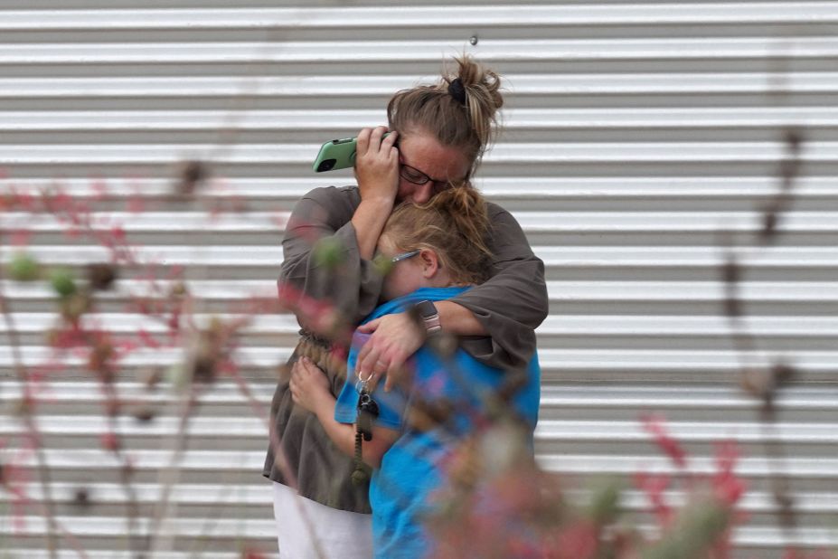 A woman cries and hugs a young girl while on the phone outside the civic center in Uvalde.