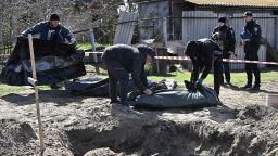 Ukrainian police observe as municipal workers place into body bags two bodies exhumed from graves dug in the yard of a house, in the village of Vablia, Kyiv Oblast, on April 14, 2022, amid Russia's invasion launched on Ukraine. 