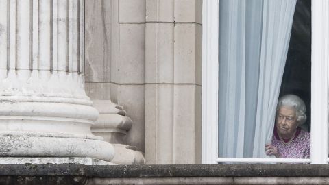 The monarch peers through the curtains of Buckingham Palace as she waits for the Patrons Lunch to start on the Mall in central London on June 12, 2016.