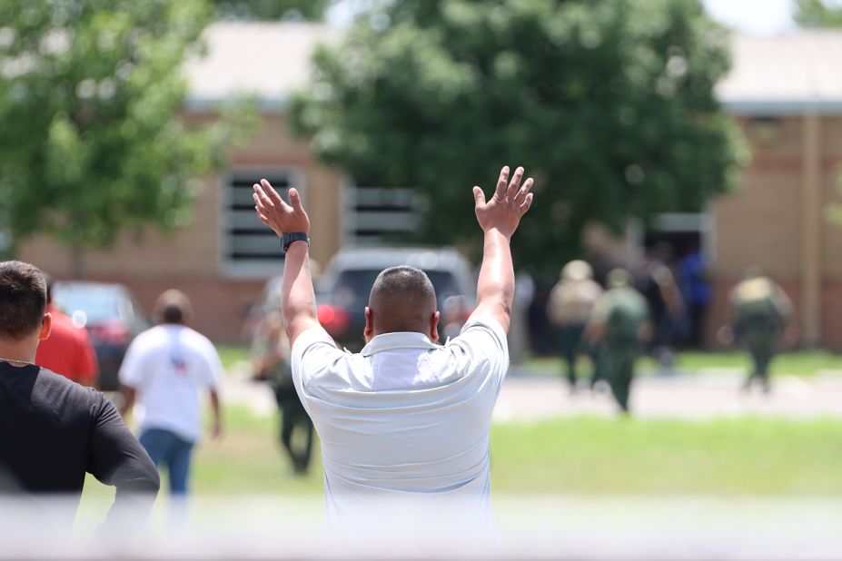 A man throws his hands in the air as students are helped to safety.
