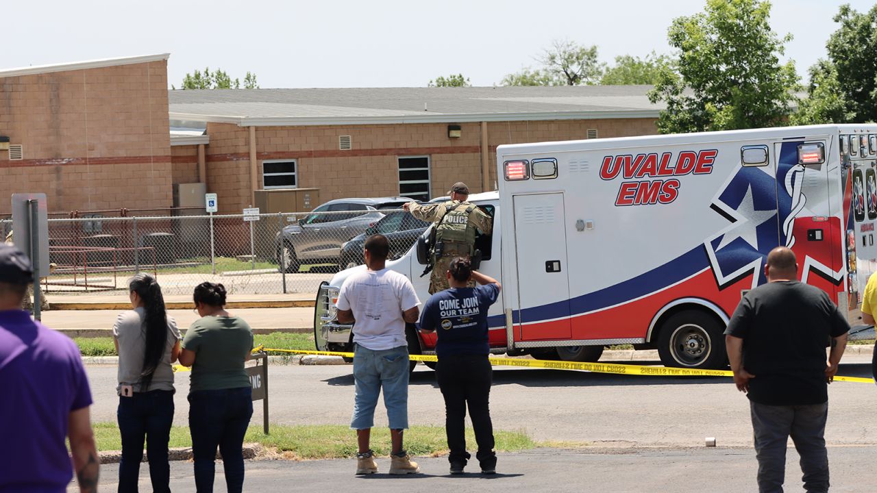 An ambulance waits at Robb Elementary School as people watch from behind police tape in Uvalde, Texas, on May 24, 2022.