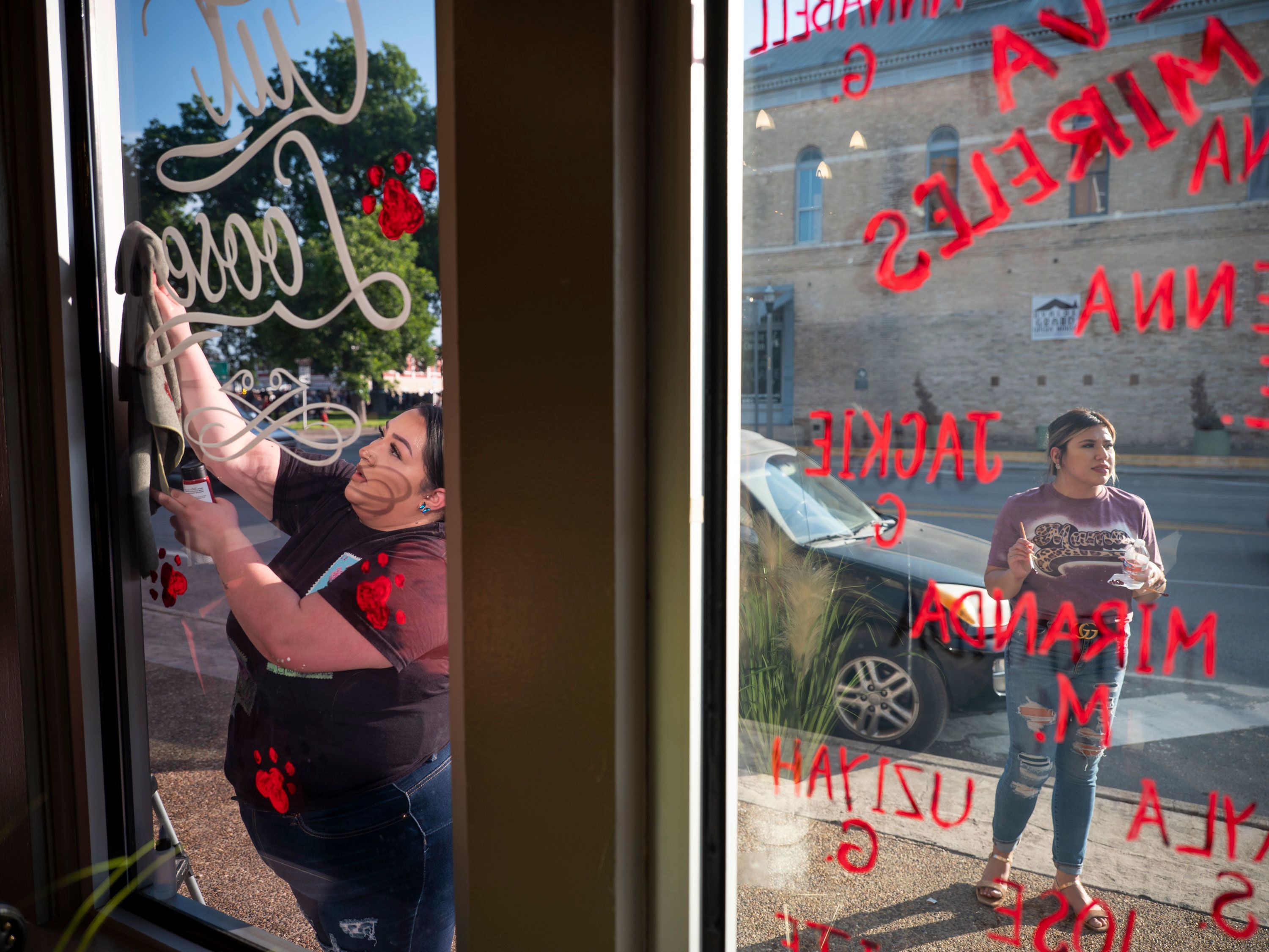 Vanessa Palacios, left, and Melissa García write the names of shooting victims on their storefront in Uvalde, Texas, on Friday, May 27.