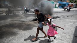 FILE - A woman and child run past burning barricades during a demonstration against increasing violence in Port-au-Prince, Haiti, March 29, 2022. The protest coincides with the 35th anniversary of Haiti's 1987 Constitution and follows other protests and strikes in recent weeks in the middle of a spike in gang-related kidnappings. 