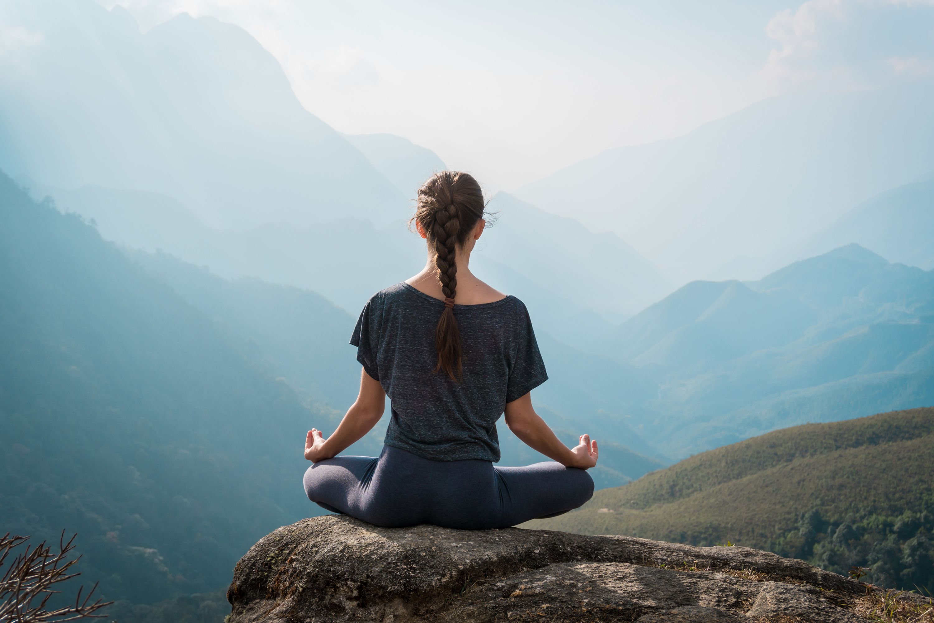 woman meditating on the edge of a mountain