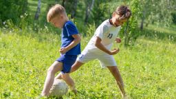 two boys play soccer on the field on a sunny summer day