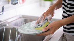female hand gesture cleaning plate using sponge and soap in the kitchen sink