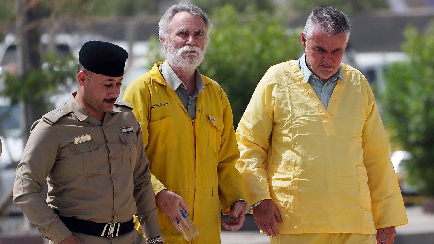 Volker Waldmann, right, and Jim Fitton, center, are handcuffed as they walk to a courtroom escorted by police arriving to court in Baghdad, Iraq, Sunday, May 22, 2022. Waldmann and Fitton have been accused of smuggling ancient shards out of Iraq.