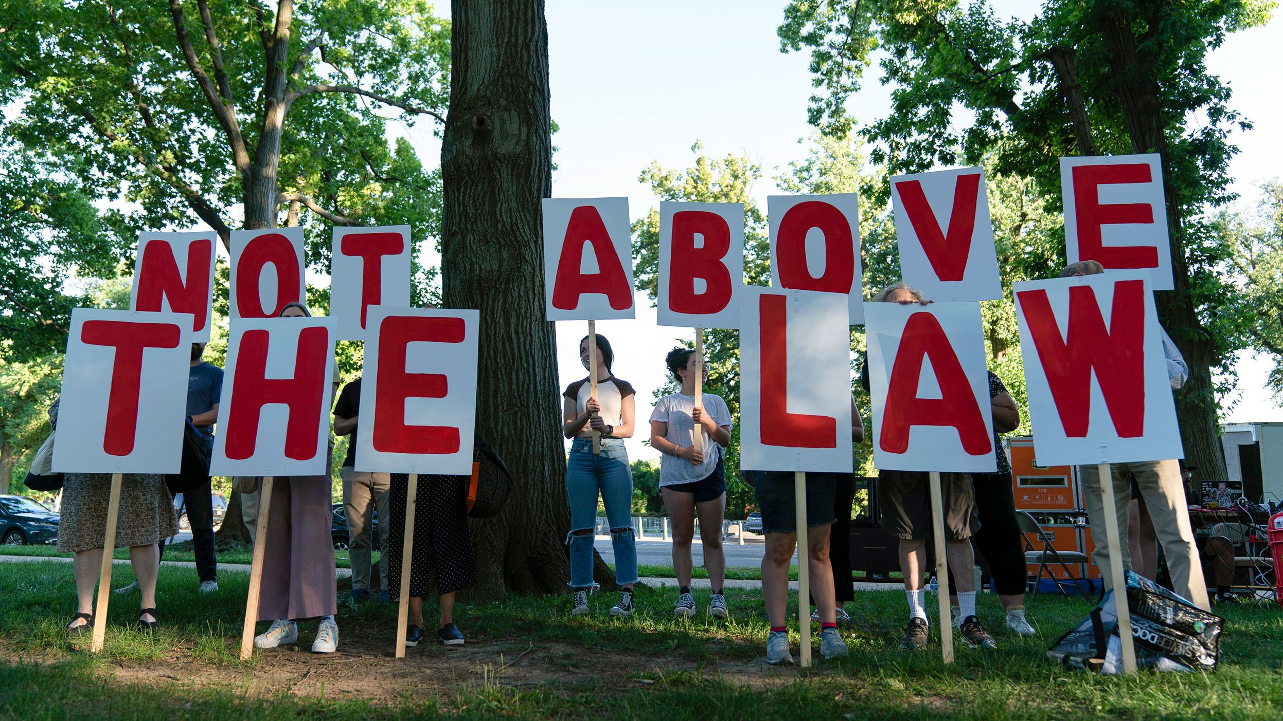 Demonstrators holds signs that say "not above the law" as they rally before the first hearing.