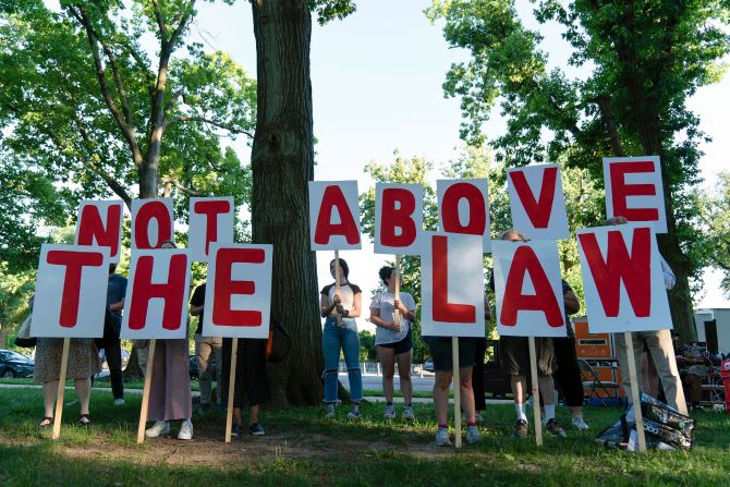 Demonstrators holds signs that say "not above the law" as they rally before the first hearing.