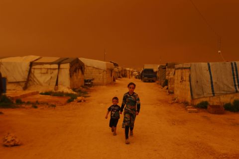 Displaced children walk past tents during a dust storm Thursday, June 2, on the outskirts of the rebel-held town of Dana, Syria.