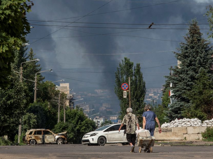 Local residents walk along an empty street as smoke rises in the background in the town of Lysychansk, Ukraine, on June 10.