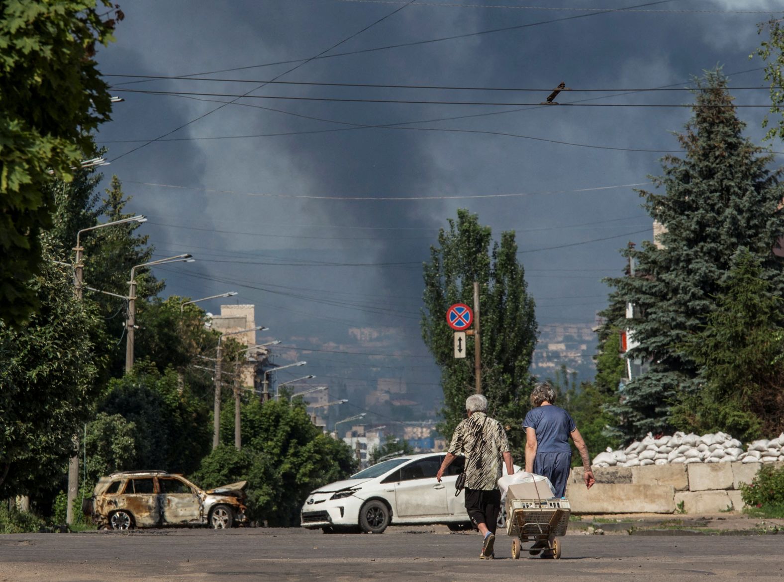 Local residents walk along an empty street as smoke rises in the background in the town of Lysychansk, Ukraine, on June 10.