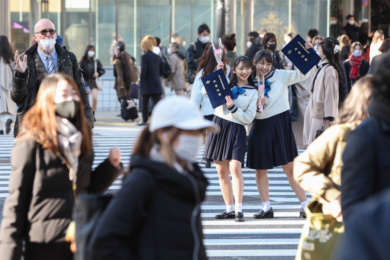 High school girls in uniform take photos with their graduation certificates in central Tokyo.