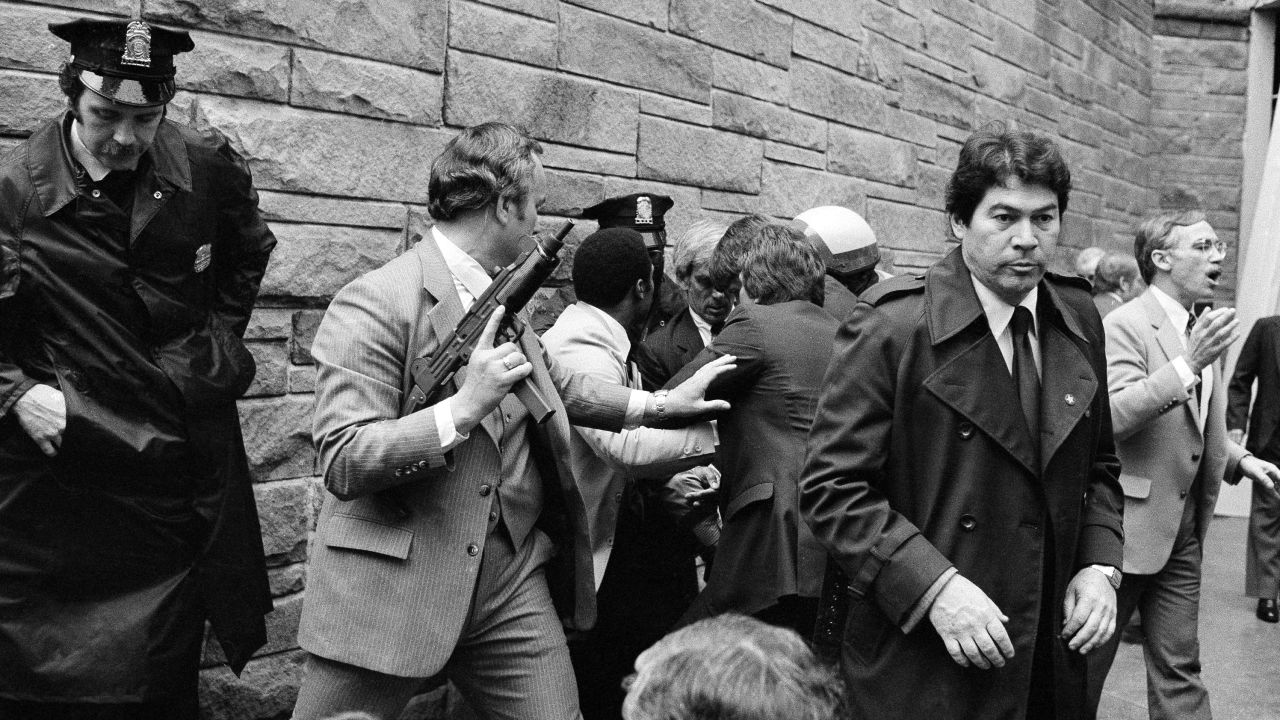Secret Service agents and police officers swarm John Hinckley Jr., obscured from view, after he attempted an assassination on President Ronald Reagan outside the Washington Hilton hotel on March 30, 1981. 