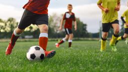 Soccer player kicking ball in game. Group of School kids playing football on grass field.