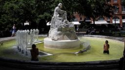 A pedestrian walks past as children play in a fountain in the city centre of Toulouse, south-western France, on June 16, 2022. - France is set to face the earliest heat wave ever recorded by weather service Meteofrance places 25 departments under orange level heat wave alert and 12 under the red level, the highest level of alert. (Photo by Lionel BONAVENTURE / AFP) (Photo by LIONEL BONAVENTURE/AFP via Getty Images)