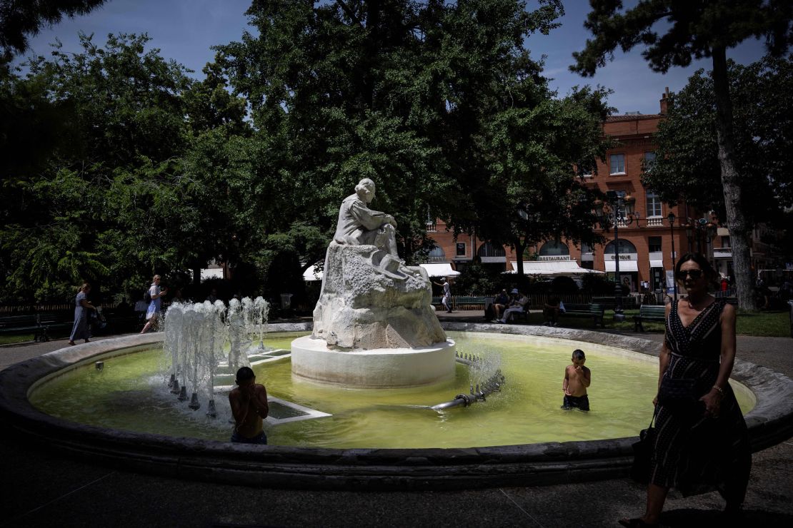 A pedestrian walks past as children play in a fountain in the city centre of Toulouse, south-western France, on June 16, 2022. 